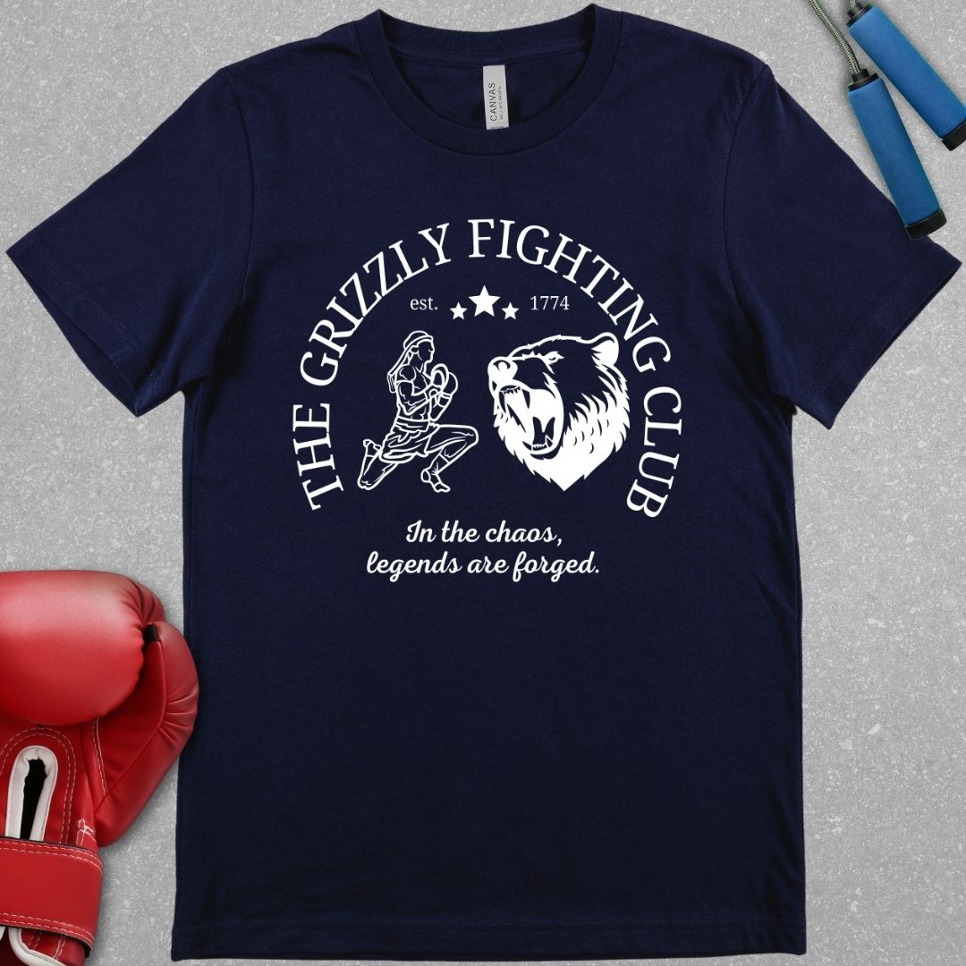 Navy shirt with a white design. The design has the words The Grizzly Fighting Club and has a Muay Thai guy doing the Wai Khru next to a Grizzly bear. At the bottom of the design has the words In the Chaos, legends are forged.