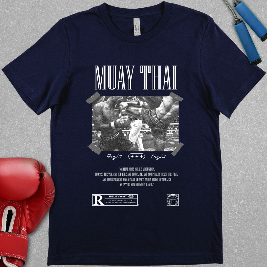 Navy shirt with a design that has a picture of two Muay Thai fighters fighting each other. Below the picture is the words Fight Night and the phrase - Martial arts is like a mountain, you see the top, and you hike and you climb, and you finally reach the peak, and you realize it was a false summit, and in front of you lies an entire new mountain range.